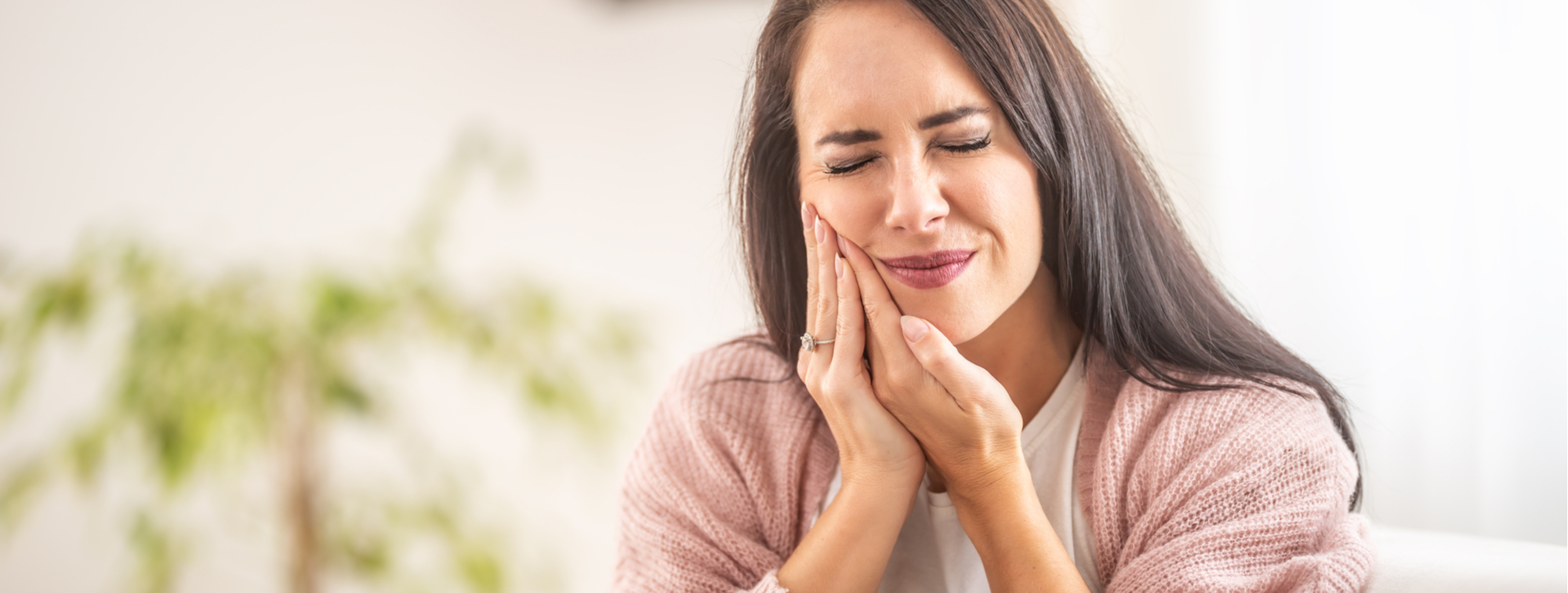 Woman holding Cheek in Pain Wearing Pink Sweater in Need of Dental Emergency Services