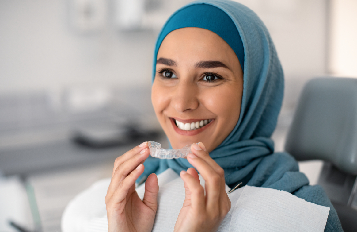 woman sitting in a dental chair holding her Invisalign aligner trays