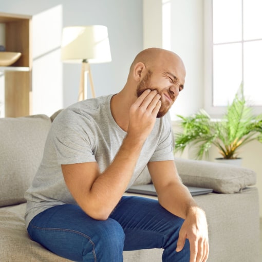 Man in Need of Wisdom Teeth Removal Sitting on Couch With Teeth Pain