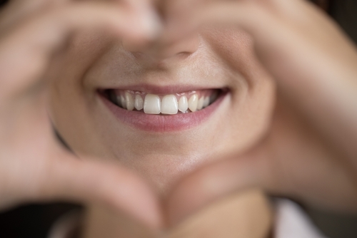Woman Making Heart Sign Showing Straight Teeth - good dental habits