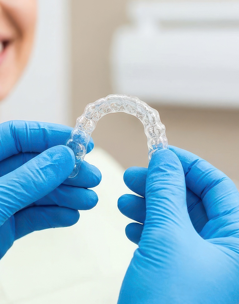 Dentist holding clear plastic dental aligner in front of smiling female patient during orthodontic treatment.